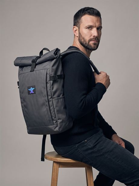 Grey roll-top backpack, seated on a stool — AI-generated product photo, same male model, frame 5 of 25